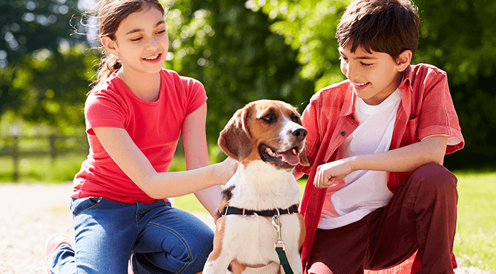 two kids in red shirts petting their dog outside